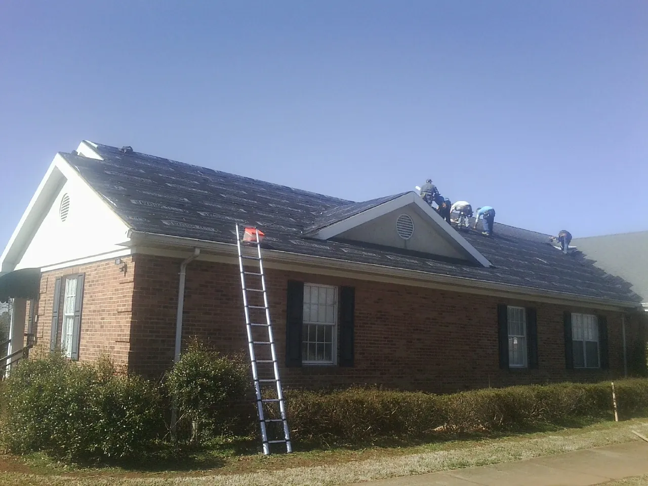 Crew tearing shingles off a brick ranch roof with a ladder set — Emergency Roof Repair work by our crew in Nicholson