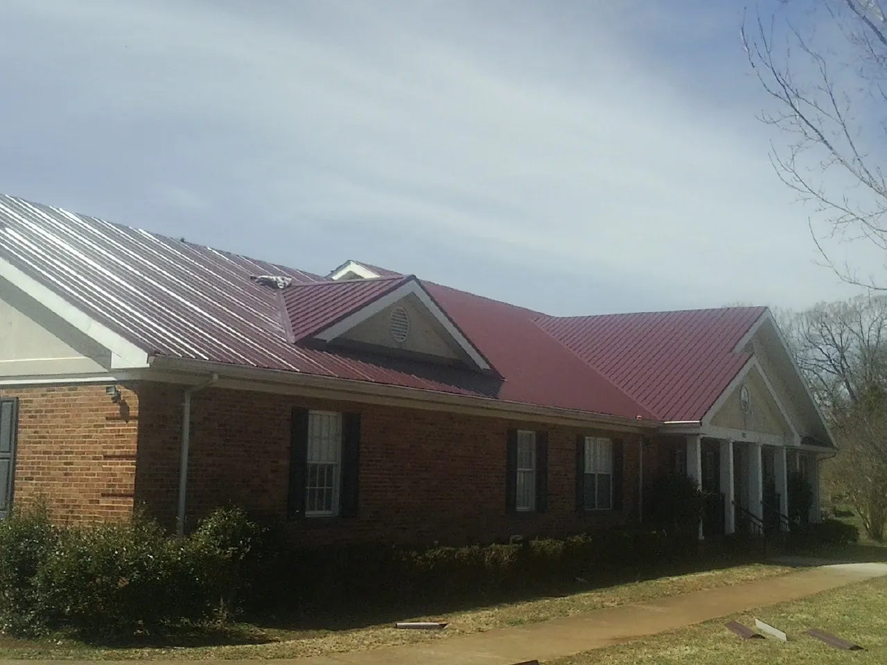 Red metal roof with gabled entries on a long brick building, from a Hail Damage Roof Repair job in Nicholson