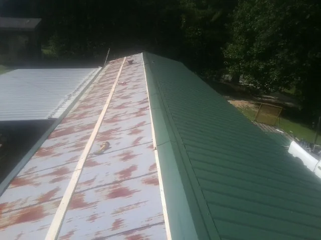 Old rusted panels beside newly installed green metal roofing — Wind Damage Roof Repair by Roofing Brothers in Nicholson