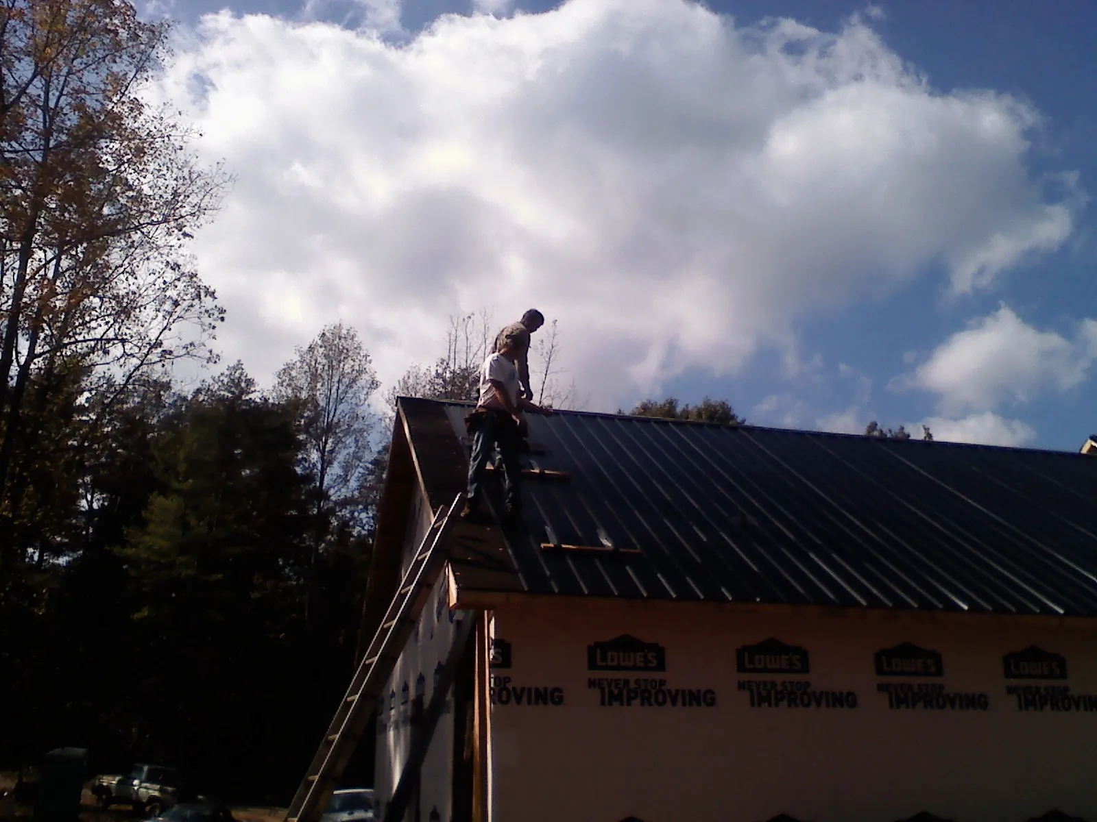 Roofer fastening dark metal panels high against a cloudy sky, from a Roof Inspection job in Nicholson