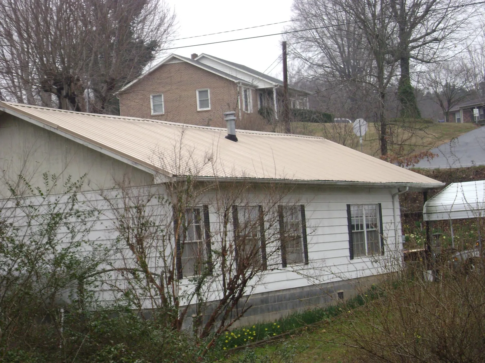Tan metal roof on a white sided house set into a hillside — Commercial Roofing by Roofing Brothers in Nicholson