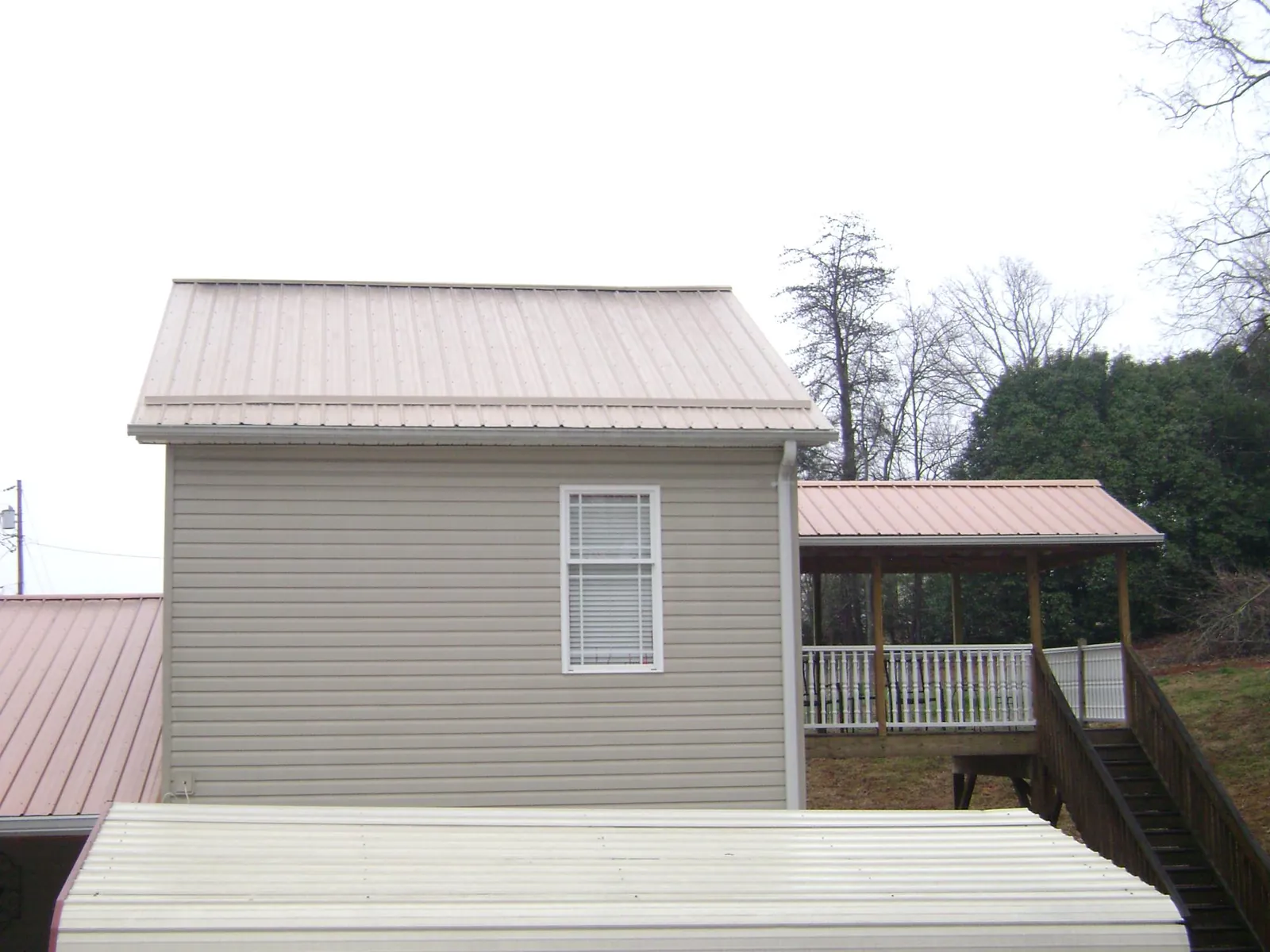Tan metal roofs on a two story addition and attached porch, from a Roof Replacement job in Nicholson